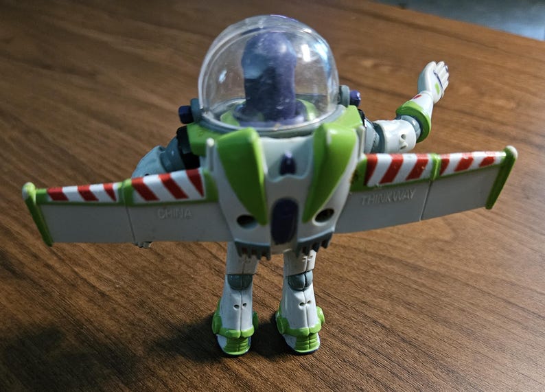 Puede incluir: Figura de acci&oacute;n de Buzz Lightyear, con casco transparente, traje espacial verde y blanco, y alas a rayas rojas y blancas. El juguete est&aacute; posando con un brazo levantado y las alas extendidas.