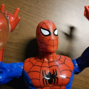 以下が含まれることがあります： 赤と青のコスチュームを着たスパイダーマンのアクションフィギュア。黒いクモのエンブレムとクモの巣のディテールが特徴です。フィギュアは白い目を持ち、透明な円形のウェブシューターを持っています。コレクションアイテムです。