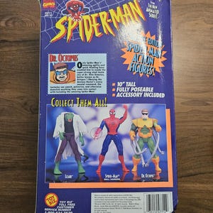 以下が含まれることがあります： ヴィンテージのスパイダーマンのアクションフィギュアの箱。箱にはスパイダーマンのロゴと、スパイダーマン、ドクター・オクトパス、リザードのアクションフィギュアの画像が描かれています。箱の高さは25.4cmで、アクセサリーが含まれています。