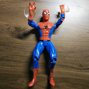 以下が含まれることがあります： ダイナミックなポーズの、赤と青のコスチュームを着たスパイダーマンのアクションフィギュア。ウェブシューター付き。胸にクモのエンブレムとマスクが付いた、詳細なデザインです。フィギュアの高さは約15cmです。