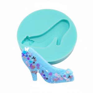 May include: A light blue silicone mold in the shape of a high-heeled shoe. A completed light blue high-heeled shoe with glitter and star-shaped embellishments is next to the mold. The shoe has a pointed toe and a high heel.