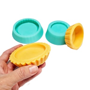 Pode incluir: Três moldes de silicone para fazer bolos ou tartes pequenos. Dois moldes são azul turquesa e um é amarelo. O molde amarelo tem uma borda canelada.