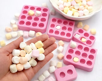 Puede incluir: Moldes de silicona rosas con múltiples hendiduras circulares llenas de malvaviscos coloridos. Una mano sostiene un montón de malvaviscos de varios colores pastel. Un cuenco blanco está lleno de malvaviscos.