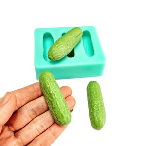 May include: A green silicone mould with three cavities shaped like cucumbers. Three green cucumber-shaped sweets are shown next to the mould.