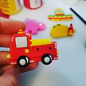 May include: A red fire truck with a yellow ladder, white wheels, and a white star on the side. The truck has glitter on the front window and white dots around the edges.