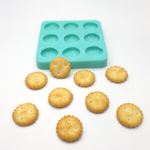 May include: A turquoise silicone mould with 12 round cavities, and nine round crackers on a white surface.