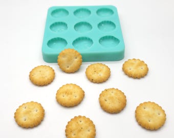 May include: A turquoise silicone mold with 12 round cavities, and nine round crackers on a white surface.