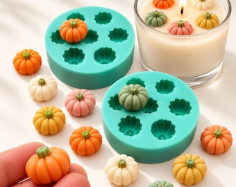 May include: Two round teal silicone moulds for casting small pumpkin shapes, accompanied by numerous miniature pumpkin figurines in orange, yellow, white, pink, and sage green, plus a glass candle with several pumpkins on the wax surface.