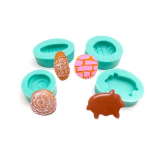 May include: A selection of teal silicone moulds with various resin castings. The castings feature an oval with a textured pattern, a pink and orange brick design, a spiral, and a brown pig shape.