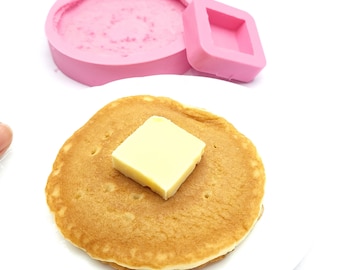Puede incluir: Un panqueque redondo de color marrón dorado con una porción de mantequilla en la parte superior. El panqueque está en un plato blanco.
