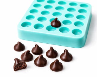 Puede incluir: Un molde de silicona turquesa con 35 cavidades circulares, junto con una dispersión de chispas de chocolate negro. Una chispita descansa en una cavidad, y otra está cortada, revelando su interior. Las chispas tienen una forma clásica de lágrima.