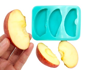 May include: A turquoise silicone mold with three half-circle shapes. Three red apple slices are next to the mold.