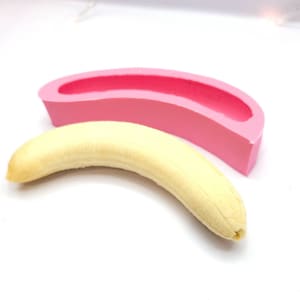 Peut inclure: Un moule en silicone rose en forme de banane, à côté d'une vraie banane.