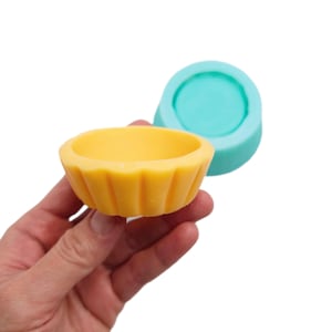 Könnte beinhalten: Eine gelbe Silikonform in Form einer Cupcake-Förmchen, neben einer blaugrünen Silikonform in Form einer runden Kuchenform.