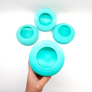 May include: Four turquoise silicone lids for food storage containers. The lids are round and have a raised lip around the edge.