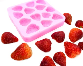 Puede incluir: Molde de silicona rosa con 12 cavidades en forma de corazón, diseñado para crear golosinas con forma de fresa. Alrededor del molde hay 11 fresas rojas frescas.