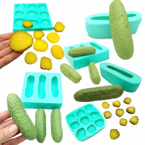 以下が含まれることがあります： ピクルス型のスイーツを作るためのシリコンモールドのセット。モールドはターコイズブルーで、さまざまなサイズと形があります。画像には、リアルなピクルス型のキャンディーもいくつかあります。
