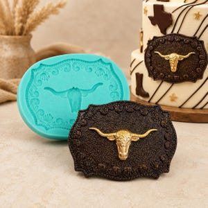 May include: A turquoise silicone mould and a brown, gold-toned, decorative cake topper featuring a longhorn design. The cake topper is a detailed, textured oval shape with a gold longhorn head in the centre. A decorated cake is in the background.