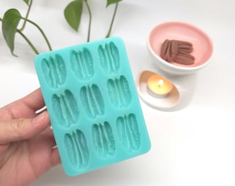 May include: A rectangular light blue silicone mold featuring nine recessed cavities shaped like pecan nut halves. The mold has a smooth, flexible texture and is designed for casting or molding small items in the shape of textured nuts.