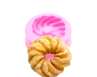 May include: Pink silicone donut mould with a golden brown donut with powdered sugar.