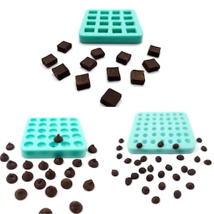 May include: Two turquoise silicone moulds, one with square cavities and the other with round cavities. The square mould is filled with small, dark brown chocolate squares. The round mould is filled with small, dark brown chocolate chips. There are also loose chocolate squares and chips scattered around the moulds.