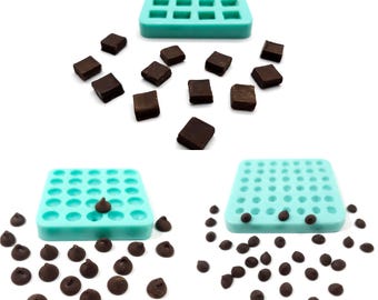 May include: Two turquoise silicone molds, one with square cavities and the other with round cavities. The square mold is filled with small, dark brown chocolate squares. The round mold is filled with small, dark brown chocolate chips. There are also loose chocolate squares and chips scattered around the molds.