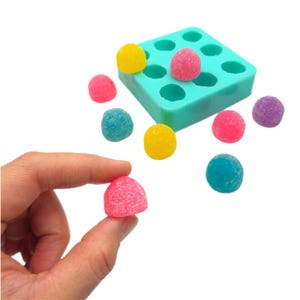 May include: A teal silicone mould with 12 round cavities, filled with colourful gummy sweets. The sweets are scattered around the mould, including pink, yellow, blue, and purple.