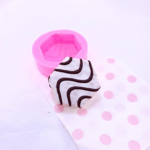 May include: A pink silicone mould shaped like a hexagon, with a white and black striped cake inside. The cake is sitting on a white napkin with pink polka dots.