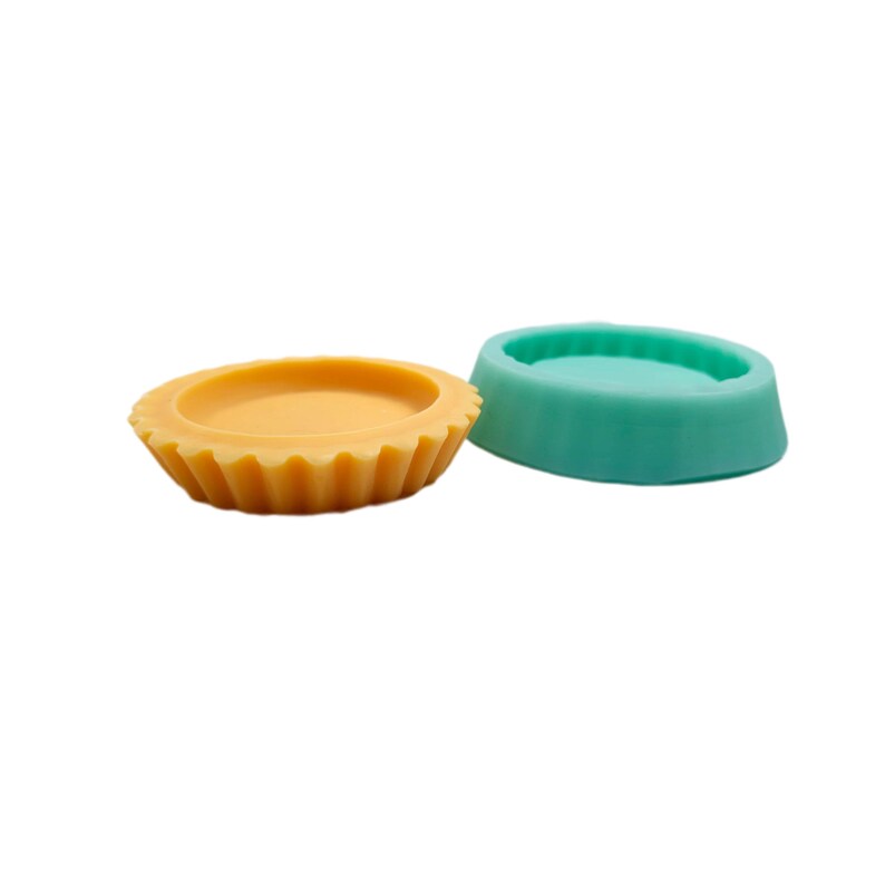 Op de afbeelding: Twee ronde siliconen mallen voor het maken van kaarsen of zeep. De mal aan de linkerkant is geel en heeft een gegolfde rand. De mal aan de rechterkant is turquoise.