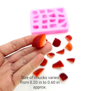 May include: A hand holding a fresh strawberry chunk, with other strawberry pieces scattered nearby. A pink silicone mold with geometric shapes is in the background. Text on the image reads: "Size of chunks varies from 0.5 cm to 1.5 cm approx."