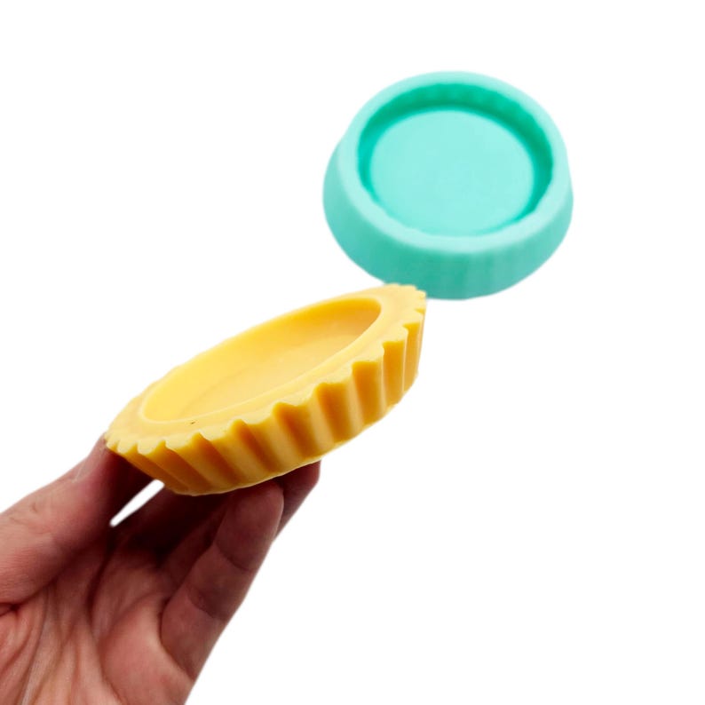 Op de afbeelding: Twee siliconen mallen voor het maken van kleine taarten of taartjes. E&eacute;n mal is geel en heeft een gegolfde rand. De andere mal is turquoise blauw en heeft een gladde rand.