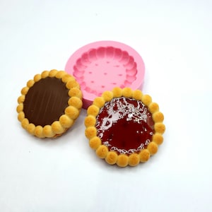May include: Two round cookies with a chocolate and a red jelly filling, and a pink silicone mould for making cookies.