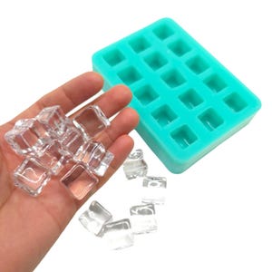 Könnte beinhalten: Eine türkisfarbene Silikon-Eiswürfelschale mit quadratischen Formen neben einer Handvoll klarer Eiswürfel. Die Eiswürfel sind quadratisch und scheinen frisch zubereitet zu sein. Die Schale ist leer und einsatzbereit.
