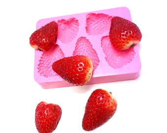 Puede incluir: Molde de silicona rosa con seis cavidades en forma de fresa. Se muestran cinco fresas rojas frescas, una en el molde y cuatro fuera del molde.