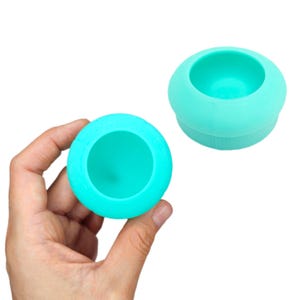 May include: Two turquoise silicone cups, one in a hand and the other on a white background. The cups are round and have a smooth, glossy finish.