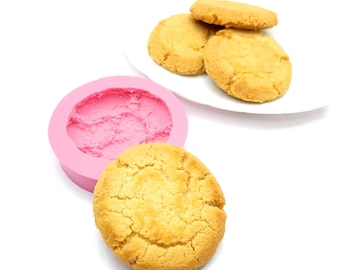 May include: A pink silicone mold for baking cookies, with four golden brown cookies on a white plate.