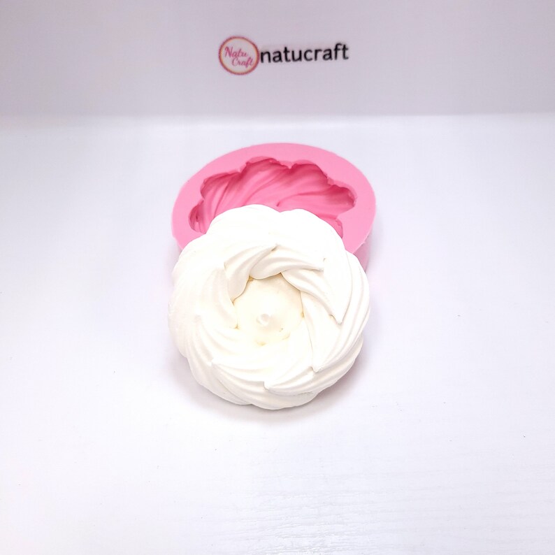 Op de afbeelding: Een wit, spiraalvormig decoratief item naast een roze siliconen mal. De mal heeft de vorm van een bloem. Het logo "Natucraft" staat in de rechterbovenhoek.