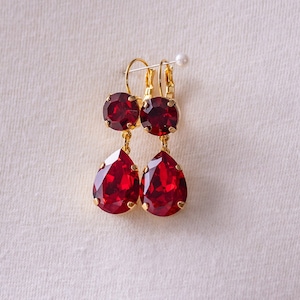 May include: A pair of dangle earrings with red teardrop-shaped crystals and gold-toned metal.