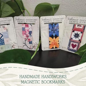 Puede incluir: Cuatro marcapáginas magnéticos hechos a mano con varios diseños. Los marcapáginas presentan patrones florales, geométricos y de estrellas en tonos de azul, rosa, rojo y naranja. Cada marcapáginas se muestra en una tarjeta blanca con el texto "HANDMADE HANDIWORKS MAGNETIC BOOKMARK".