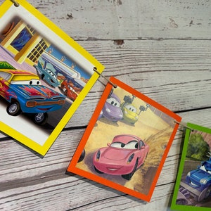 Puede incluir: Una pancarta colorida con im&aacute;genes de coches de dibujos animados de la pel&iacute;cula Cars de Disney Pixar. La pancarta est&aacute; hecha de cartulina y tiene un esquema de colores amarillo, naranja, verde y azul. Los coches son todos de diferentes colores y tienen diferentes expresiones en sus caras.