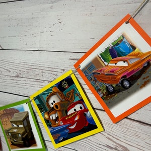 Puede incluir: Una pancarta de fiesta con tem&aacute;tica de Cars con cuadrados coloridos que presentan diferentes personajes de la pel&iacute;cula. La pancarta incluye a Mater, Rayo McQueen y otros personajes.