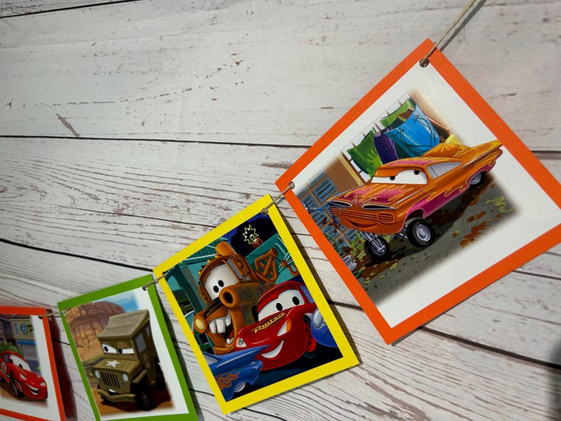 Puede incluir: Una pancarta de fiesta con tem&aacute;tica de Cars con cuadrados coloridos que presentan diferentes personajes de la pel&iacute;cula. La pancarta incluye a Mater, Rayo McQueen y otros personajes.