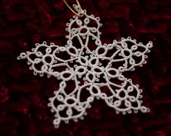 May include: A white lace snowflake ornament with a gold string for hanging. The snowflake is intricate and delicate, with many small loops and curves.