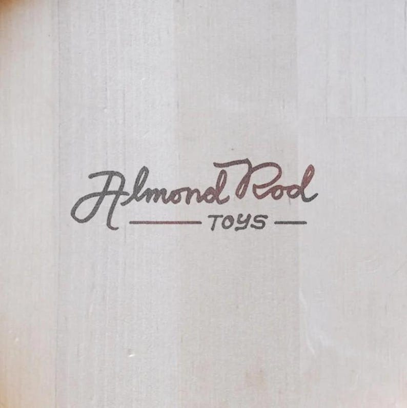 Puede incluir: Un letrero de madera blanco con escritura cursiva negra que dice "Almond Pool Toys".