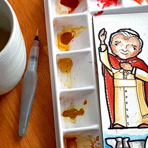 May include: A watercolor painting of a cartoon Pope wearing a white robe with a gold sash and a red cape. The painting is on a white background with a watercolor palette in the background.