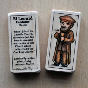 May include: Two wooden blocks with illustrations and text. One block features text about Bl Leonid Feodorov, a Russian Byzantine priest. The other block shows a watercolor illustration of a man holding a chalice and smoking a pipe.