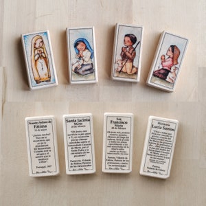 Op de afbeelding: Set van zes rechthoekige houten tegels met illustraties van religieuze figuren uit de verschijningen van Fatima. Elke tegel bevat een naam, een datum en een citaat van de figuur. De tegels zijn wit met bruine randen.