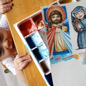 May include: A watercolor painting of Jesus Christ with a red and white robe and a blue background. The painting is on a white sheet of paper with a watercolor palette and paintbrushes in the foreground.