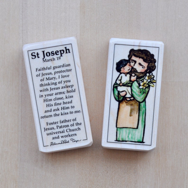 May include: A wooden bookmark with a colorful illustration of Saint Joseph holding a young child. The bookmark includes a prayer to Saint Joseph, mentioning his role as guardian of Jesus and protector of Mary. The text also mentions his role as foster father of Jesus and patron of the universal church and workers.
