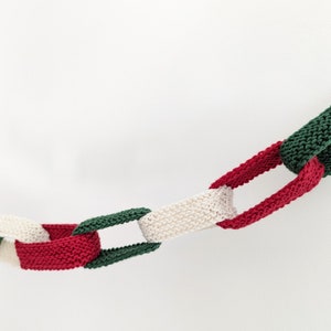 May include: A knitted garland with alternating red, white, and green sections. The garland is made of yarn and is in the shape of a chain.